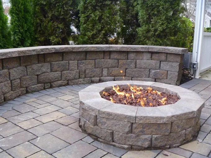 Stone gas fire pit with curved seat wall on a paver patio